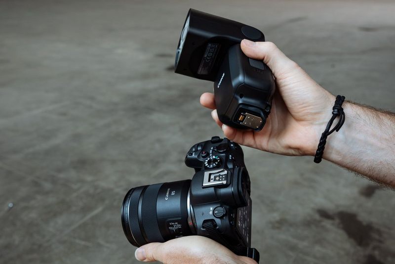 Камеру Canon и вспышку Canon Speedlite EL-5 держат в руках так, чтобы было видно многофункциональную пяту.