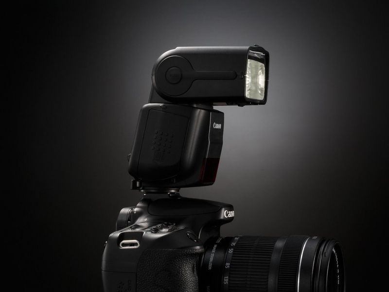 Фотография камеры Canon с установленной на нее вспышкой Canon Speedlite 430EX III-RT в профиль.
