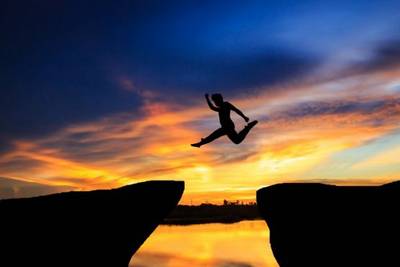 Man jumping between rocks, sunset background