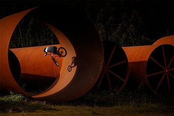 A BMX rider performs a stunt in a giant rust-coloured tube, casting a shadow against the side. Photo by Jaime de Diego.
