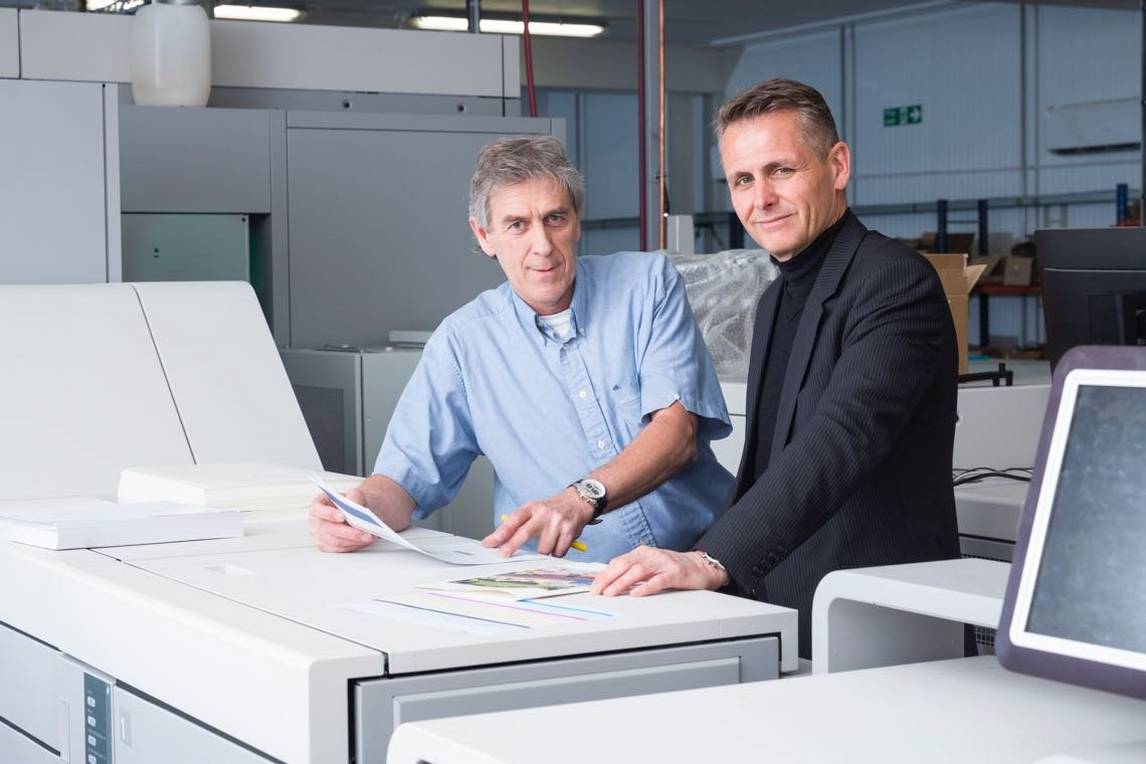 Two men examine personalised book printing pages on top of printing press