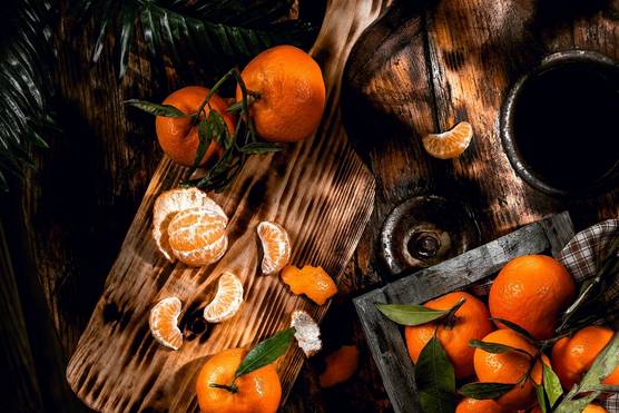 Mandarins arranged on a chopping board and tray on a dark wood table, one peeled with its segments spread out.