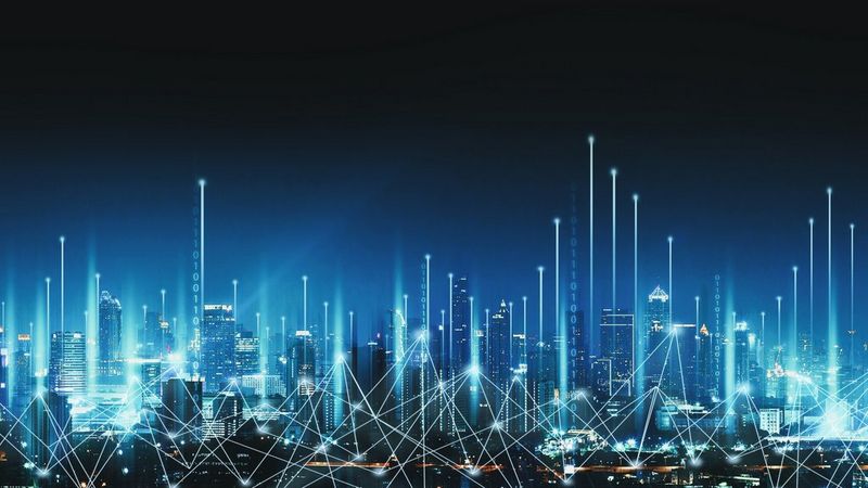 A panorama of a city at night, against a dark blue to light blue gradient background. Overlaid across the city are white connecting lines, to denote how everything is joined together in a smart city. And vertical white lights to symbolise connectivity of technology.