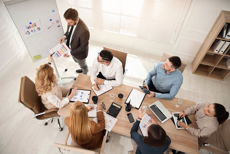 A group of people sitting in around a table in a meeting