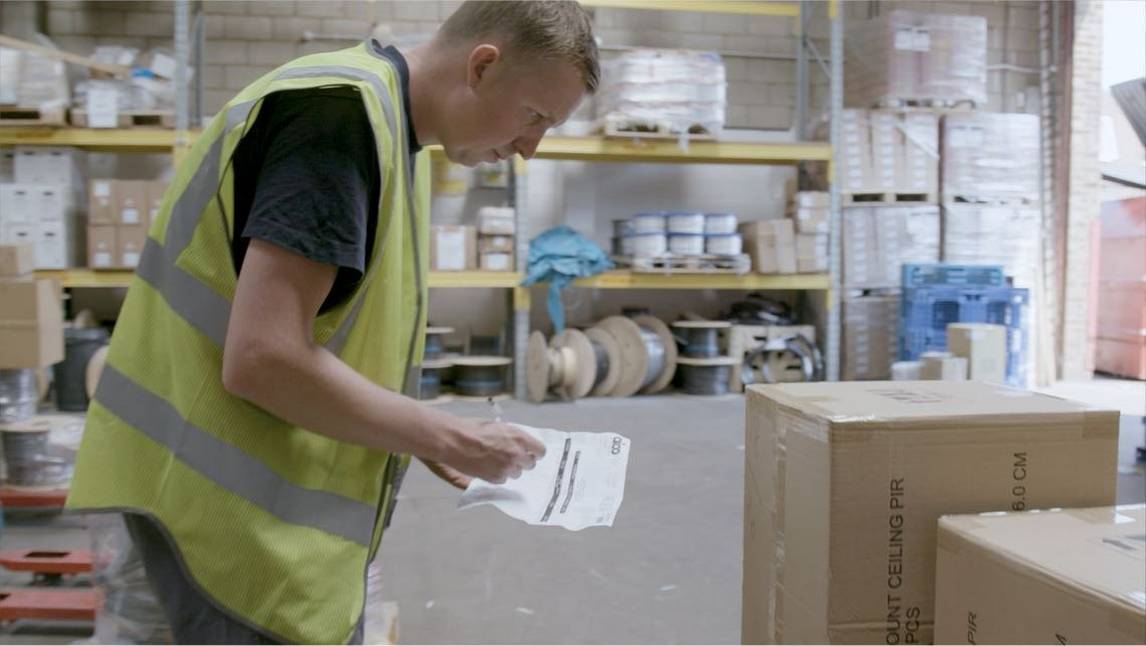 Man in high visibility vest takes stock of boxes in electrical wholesaler warehouse