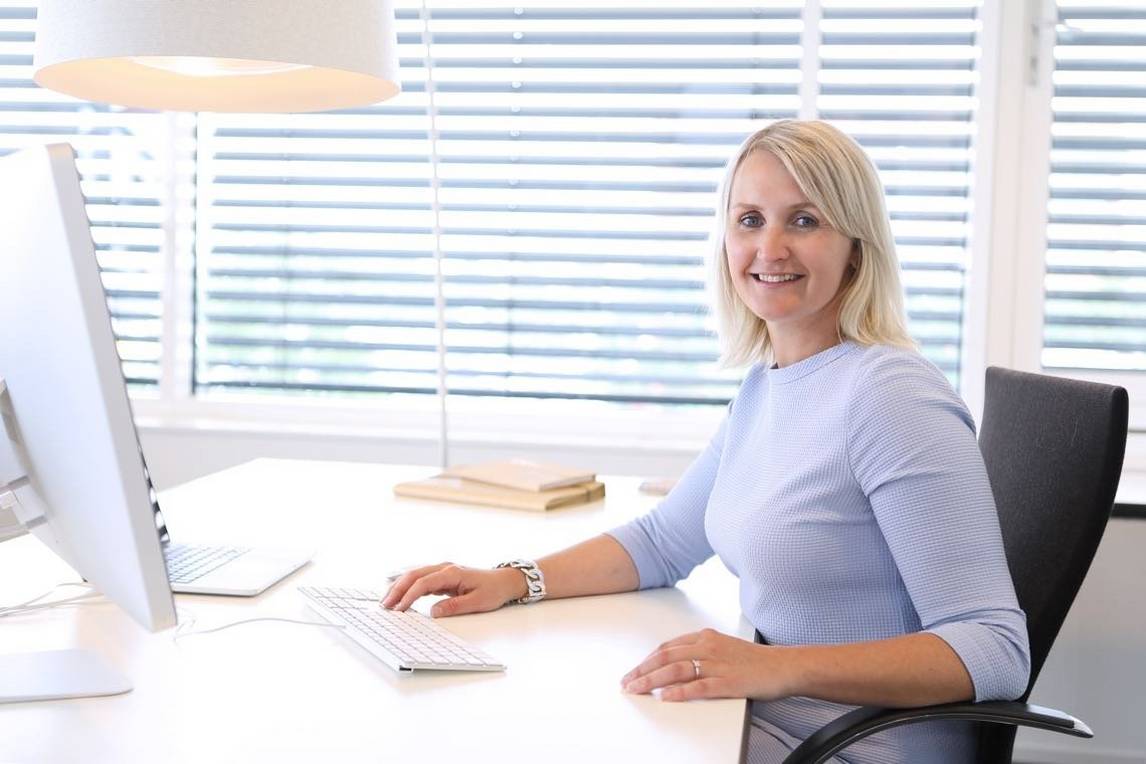 Woman sitting at office computer desk, smiling at camera