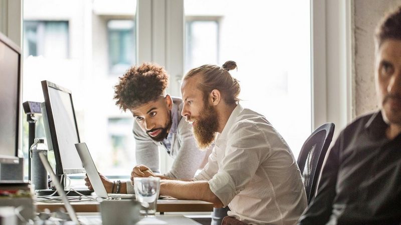 an image of two male adults looking at a laptop together in an office