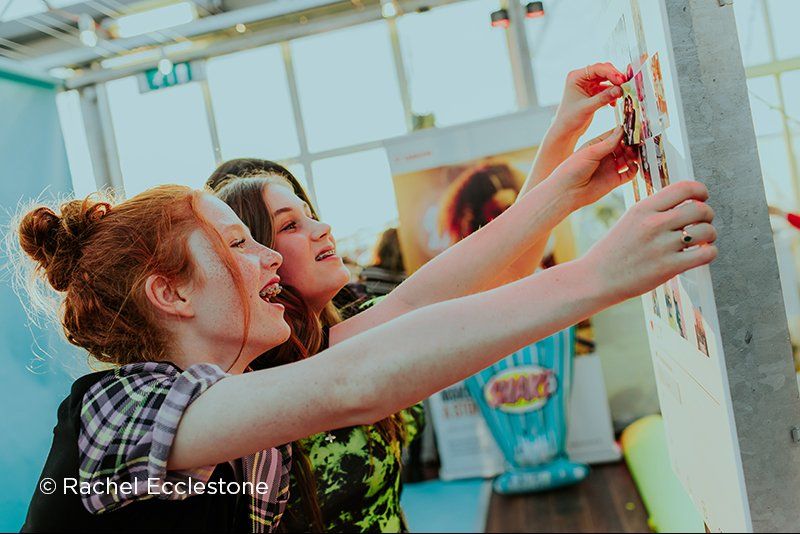 2 girls sticking printed pictures on a board.