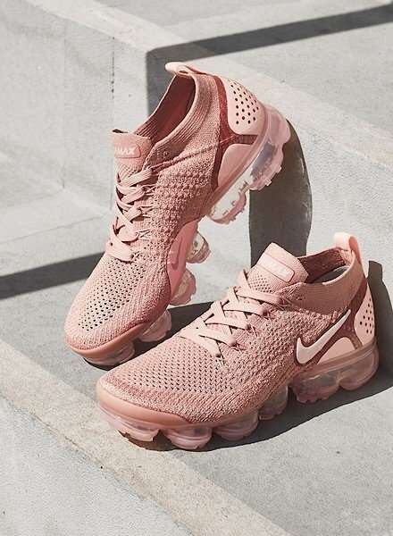 På billedet ses et par lyserøde Nike Air Vapormax sneakers. Skoene er placeret på et trappetrin af beton. Den højre sneaker er stillet op af trappetrinnet, mens den venstre står fladt på trappen. En skygge fra en lygtepæl falder i baggrunden.