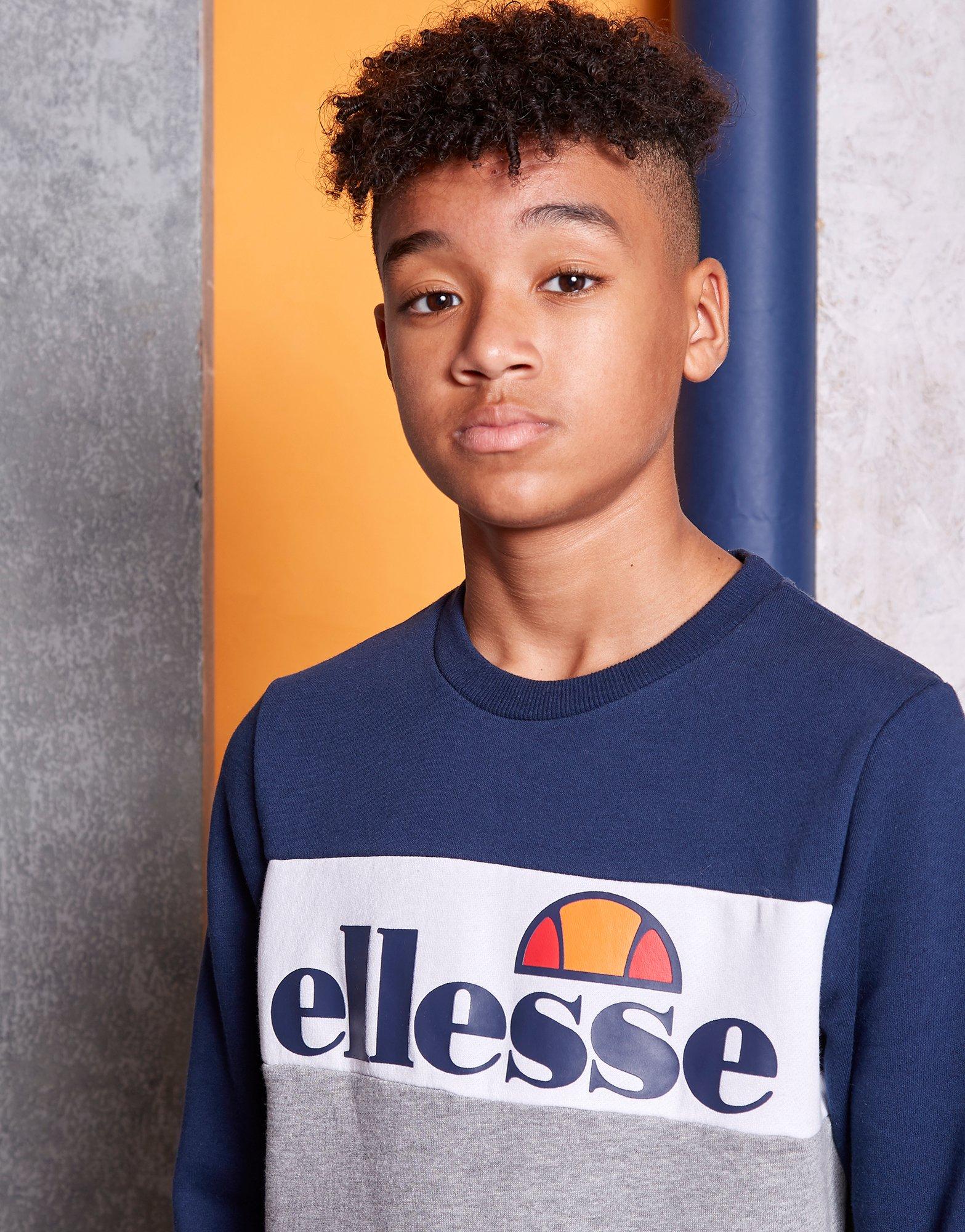 På billedet ses en ung dreng klædt i en sweatshirt fra elesse. Trøjen er blø og grå med ellesse brandet på brystet. 