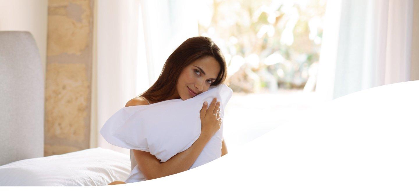 kobieta siedzi na łóżku w pościeli i przytula poduszkę